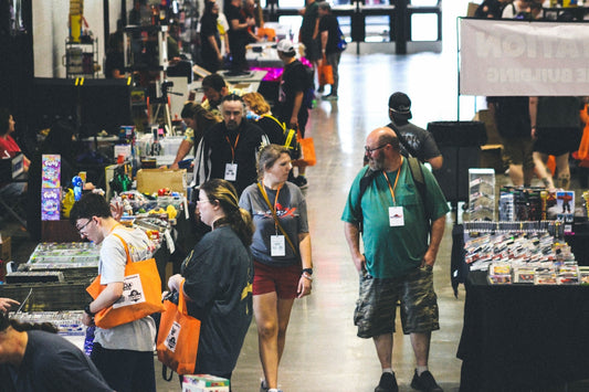 People walking through a busy indoor convention hall with booths.