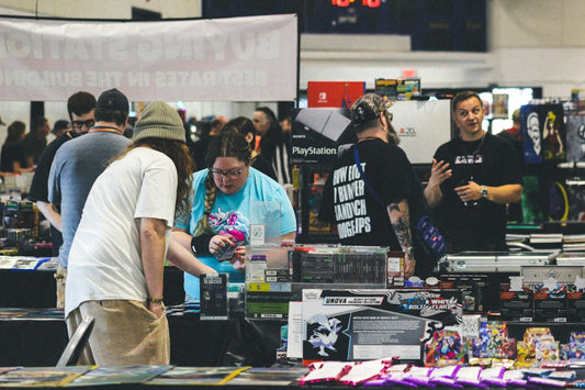 People browsing merchandise at an indoor convention or market stall.