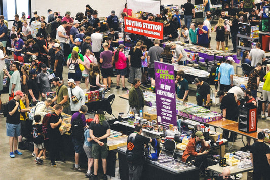 A crowded indoor convention with many people and vendor stalls.
